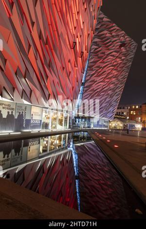 Una foto verticale del museo titanico della città di Belfast illuminata in rosso di notte Foto Stock