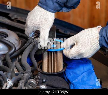 Il meccanico toglie il vecchio filtro del carburante sporco per sostituirlo nella vettura con uno nuovo Foto Stock