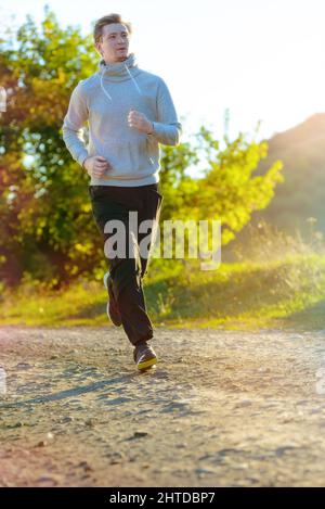 L'uomo che fa jogging nella natura rurale durante la splendida giornata estiva. Sport fitness modello caucasico etnia formazione all'aperto. Foto Stock