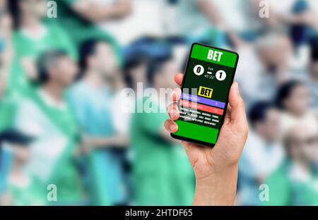 Primo piano su un uomo che tiene un telefono cellulare mentre vince una scommessa online su una partita di calcio allo stadio Foto Stock