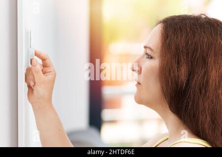 Giovane donna che accende il condizionatore d'aria mentre si trova a casa Foto Stock