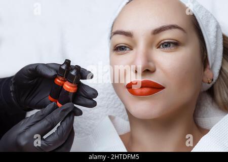 Battitura del labbro. Permanente trucco labbro cosmetologist mantiene guanti neri pigmento vernice per tatuaggio Foto Stock