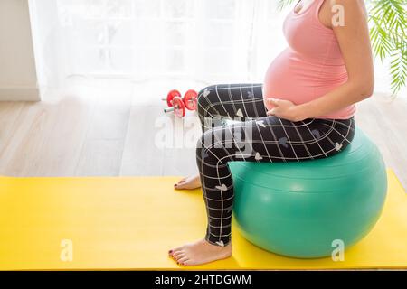 giovane donna incinta seduta su una palla fitness fa esercizi per rafforzare il pavimento pelvico in gravidanza durante le classi di preparazione del parto Foto Stock