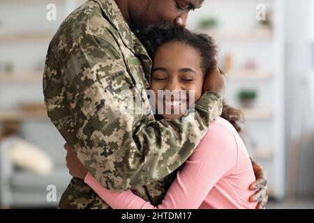 Emotiva ragazza afroamericana che abbraccia suo padre in uniforme militare Foto Stock