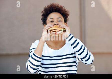 Fast food, se il mio preferito. Ritratto di una giovane donna che mangia un hamburger. Foto Stock