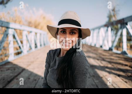 Ritratto di una donna ispanica sorridente con cappello seduto guardando la macchina fotografica Foto Stock