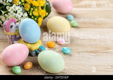 Uova di pasqua colorate, caramelle e fiori su un rustico tavolo di legno Foto Stock
