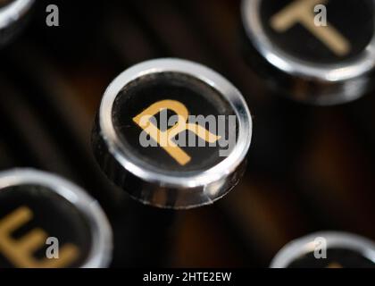 Retro macchina da scrivere d'epoca circolare chiave rotonda primo piano con lettera R color oro su sfondo nero. Foto Stock