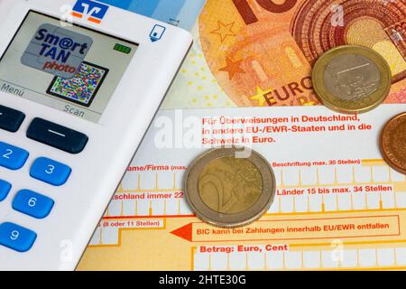 Immagine simbolo delle transazioni di pagamento: Primo piano di una polizza di bonifico bancario con monete in euro, banconote in euro e generatore TAN Foto Stock