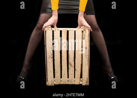 Le mani delle donne tengono una scatola di legno fra le loro gambe su uno sfondo nero. Foto Stock