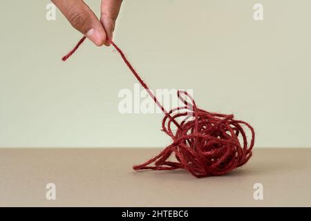 Foto ravvicinata del loop rosso e della mano che cerca di slegare. Concetto di capacità di problem solving e brainstorming su mentalità confusa. Foto Stock