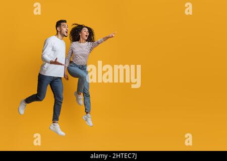 Guarda qui. Stupito la coppia araba che punta da parte mentre saltando su sfondo giallo Foto Stock