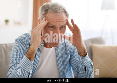 Stressato uomo maturo seduto sul divano e pensando Foto Stock