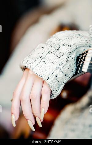 Mano femminile e chitarra acustica. Tema della riproduzione di strumenti musicali. Fotografia atmosferica ed estetica. Primo piano. Foto Stock