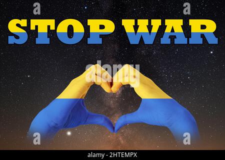 Le mani dipinte nei colori della bandiera dell'Ucraina raffigurano la forma di un cuore sullo sfondo di un cielo stellato notte e il testo STOP GUERRA. Pisello Foto Stock
