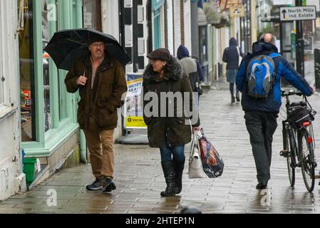 Bridport, Dorset, Regno Unito. 28th febbraio 2022. Meteo Regno Unito. Gli acquirenti si riparano sotto gli ombrelloni mentre camminano lungo il marciapiede sotto la pioggia pesante a Bridport in Dorset in un pomeriggio bagnato l'ultimo giorno dell'inverno meteorologico. Picture Credit: Graham Hunt/Alamy Live News Foto Stock