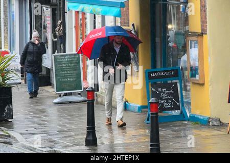 Bridport, Dorset, Regno Unito. 28th febbraio 2022. Meteo Regno Unito. Uno shopper ripara sotto un ombrello mentre cammina lungo il marciapiede nella pioggia pesante a Bridport in Dorset in un pomeriggio bagnato l'ultimo giorno dell'inverno meteorologico. Picture Credit: Graham Hunt/Alamy Live News Foto Stock