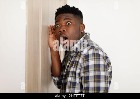 Shocked African American Man ascolto attraverso chiuso porta in piedi in interni Foto Stock