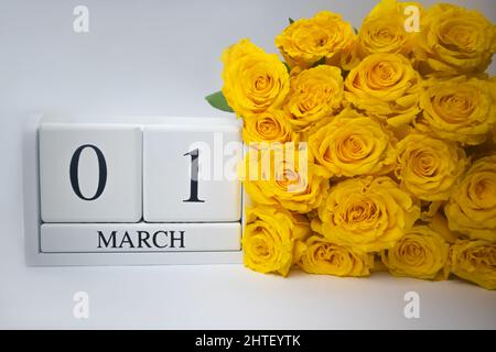 Calendario in legno Marzo 1 e rose gialle su sfondo bianco. Foto Stock