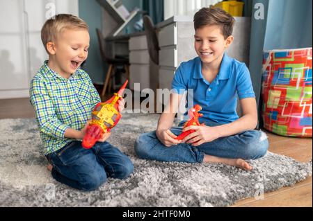 Due ragazzi con figure di animali di gomma seduti sul pavimento Foto Stock