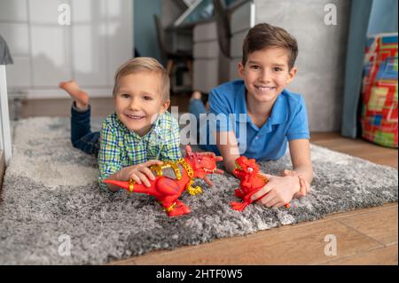 Ragazzi allegri con dinosauri giocattolo poggiati sul pavimento Foto Stock