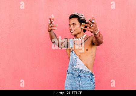 Giovane uomo che indossa un denim ballando in piedi contro la parete rosa Foto Stock