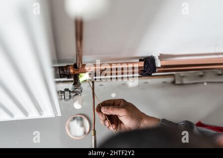 Primo piano sulle mani idraulico sconosciuto lavoratore industriale con centrale riscaldamento di tubi in rame saldatura con torcia a gas o torcia a soffiaggio accesa il muro in casa buildi Foto Stock