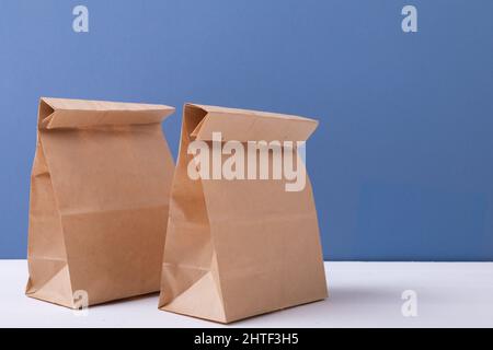 Primo piano di sacchetti di carta marroni da pranzo sul tavolo su sfondo blu con spazio per la copia Foto Stock