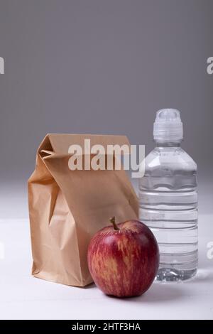 Primo piano della borsa da pranzo di carta marrone con bottiglia di mela e acqua sul tavolo su sfondo grigio Foto Stock