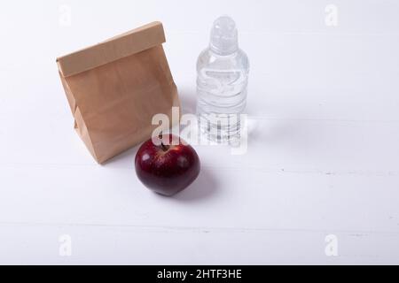 Vista ad angolo alto della borsa da pranzo di carta e mela con bottiglia d'acqua su sfondo bianco Foto Stock