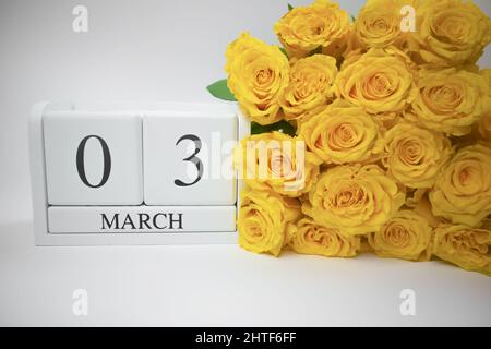 Calendario in legno Marzo 3 e rose gialle su sfondo bianco. Foto Stock