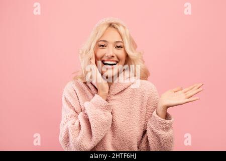 WOW, guarda qui. Giovane donna eccitato che mostra palmo aperto, mostrando spazio libero e toccando la sua guancia Foto Stock