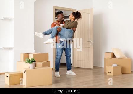 Gioioso marito afroamericano che porta moglie in Arms Standing Indoor Foto Stock