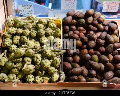 Scatole con pile di carciofi e avocado in un mercato Foto Stock