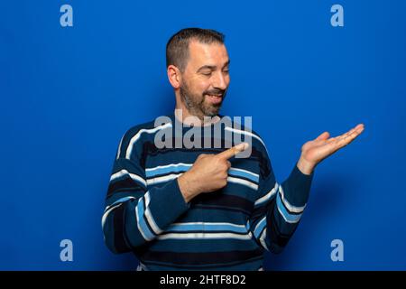 Uomo spagnolo con barba su sfondo blu isolato stupito e sorridente mentre si presenta con mano e dito puntato. Foto Stock