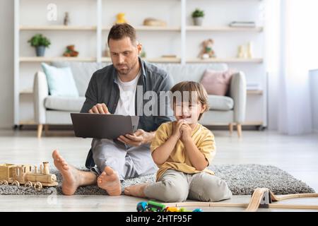 Concetto di ignoranza dei bambini. Uomo occupato che lavora su un notebook online, suo figlio piangendo da solo, sentendosi abbandonato, spazio libero Foto Stock