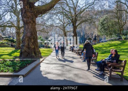 I London Memorial Gardens sono occupati di persone che camminano e si siedono su panchine lungo il percorso principale attraverso il parco. Foto Stock