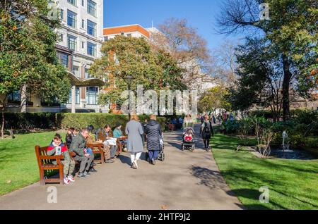 I London Memorial Gardens sono occupati di persone che camminano e si siedono su panchine lungo il percorso principale attraverso il parco. Foto Stock