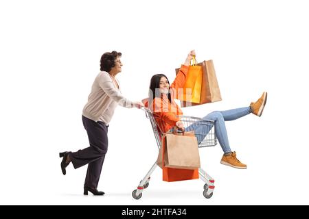 Donna anziana che spinge una giovane donna all'interno di un carrello con borse shopping isolato su sfondo bianco Foto Stock