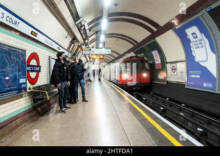 Un treno arriva al binario della stazione metropolitana di Earl's Court Londonsulla linea Piccadilly mentre i passeggeri si alzano e aspettano Foto Stock