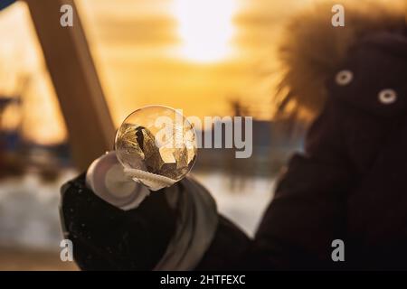 una ragazza tiene una bolla di sapone con bei modelli di gelo nei raggi del sole Foto Stock