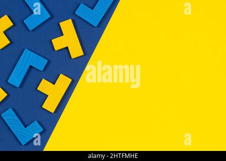 Diverse forme colorate blocchi di puzzle in legno su sfondo blu e giallo. Forme geometriche in diversi colori, vista dall'alto, spazio di copia Foto Stock