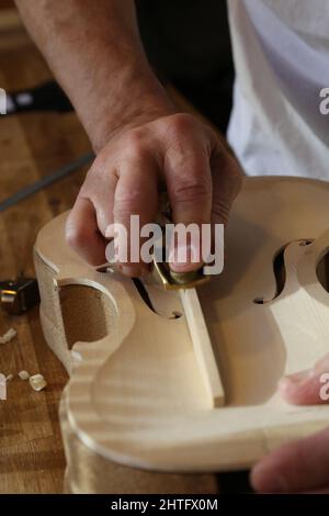 Colpo verticale di una mano dell'uomo che tiene un attrezzo per fare un violino nella sua officina Foto Stock