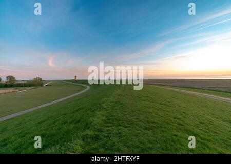 Prato verde vibrante con faro Pilsum in lontananza Foto Stock