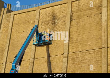 Gli uomini riparano una parete alta della scogliera sul braccio articolato Foto Stock