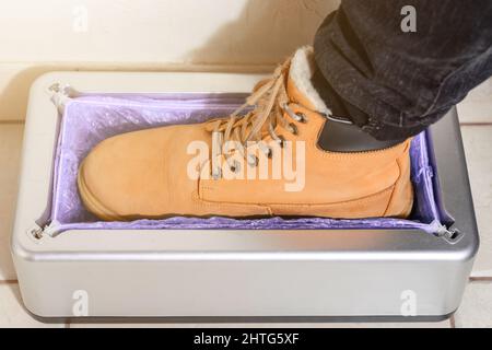 Dispositivo per la ravvivatura automatica di copriscarpe, uomo in scarpe marroni mette su copriscarpe, clintoper meccanico. Foto Stock