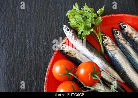 Acciughe sulla piastra res. Piccolo pesce di mare crudo e fresco, piatto adagiarsi sulla tavola nera della cucina, spazio libero per la copia Foto Stock