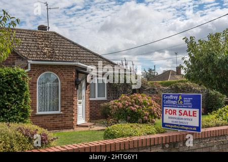 Agente immobiliare per la vendita segno fuori di un bungalow in vendita nel villaggio West Norfolk di Dersingham. Foto Stock