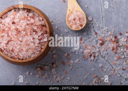 Direttamente sopra il colpo del sale rosa della roccia dell'himalaya in ciotola di legno, cucchiaio e caduto sul tavolo Foto Stock