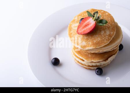 Vista ad angolo alto delle frittelle accatastate con frutta a bacca nel piatto su sfondo bianco Foto Stock